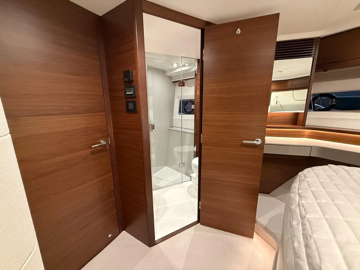 The image showcases a modern yacht interior with wooden finishes and a glimpse into a bathroom area. aboard PRINCESS 70 Yacht for Sale
