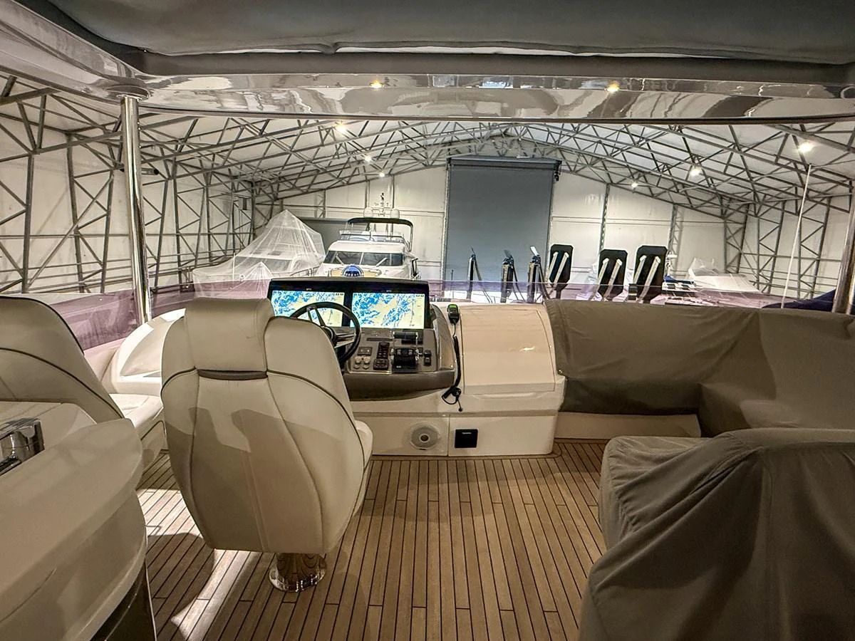 The helm station of the yacht is showcased in a covered storage area, highlighting its modern navigation equipment and comfortable seating. aboard PRINCESS 70 Yacht for Sale