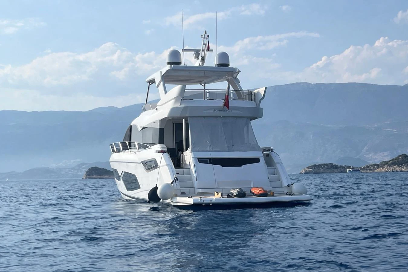 A sleek yacht is anchored in calm waters with a scenic mountainous backdrop. aboard SUNSEEKER 66 MANHATTAN Yacht for Sale