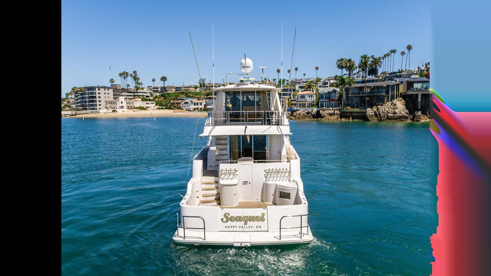 The yacht is seen from the rear, cruising in a serene coastal area with clear blue waters and a picturesque shoreline. aboard SEAQUEL Yacht for Sale