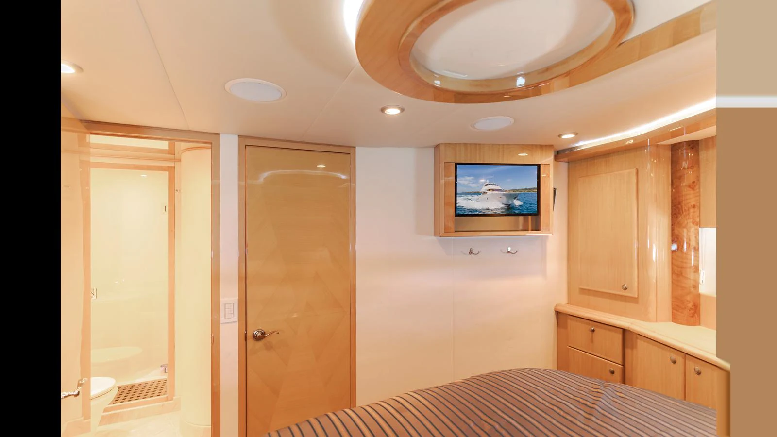 A cozy stateroom featuring a mounted TV, wooden cabinetry, and an ensuite bathroom. aboard SEAQUEL Yacht for Sale