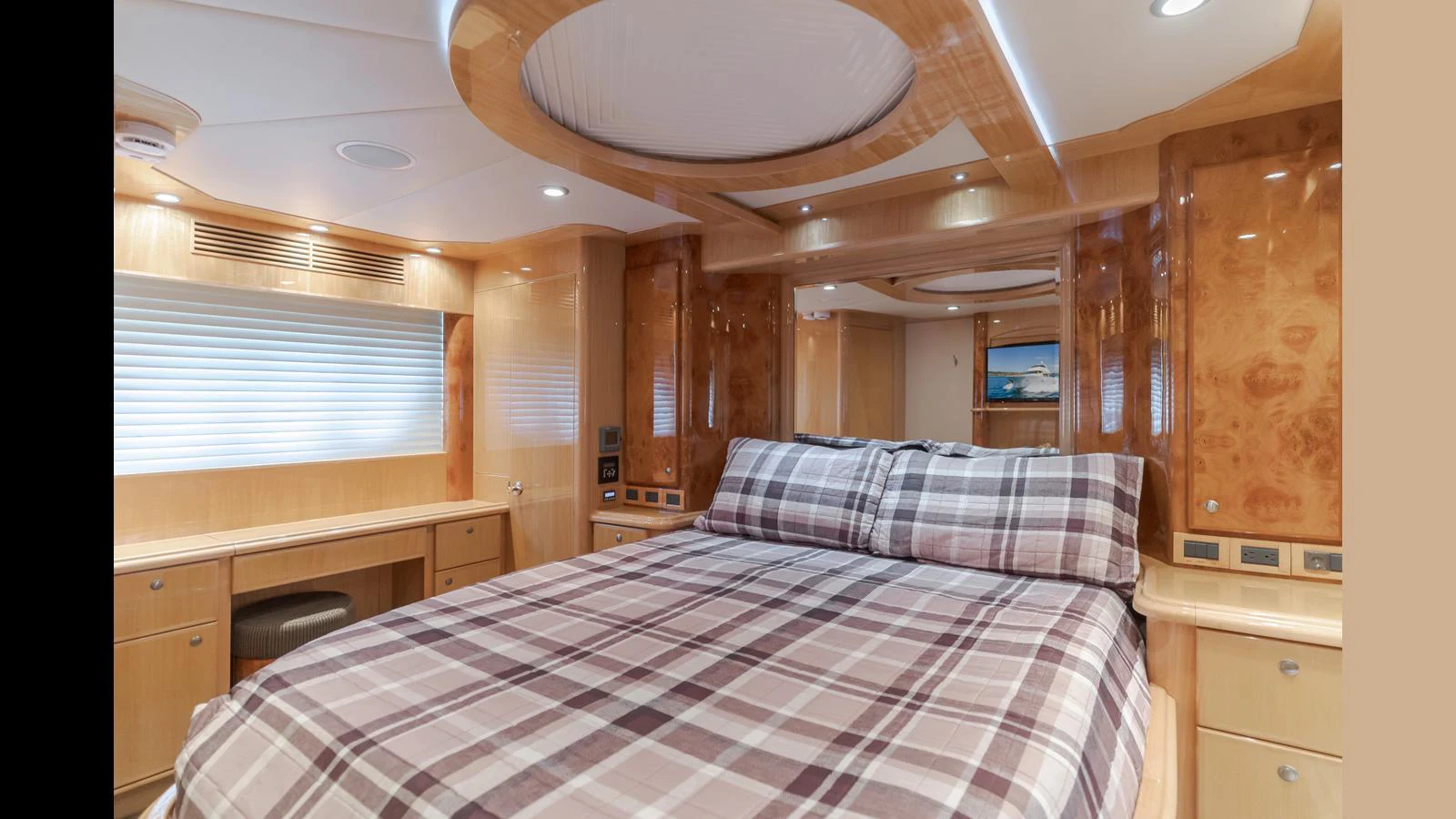 The master stateroom features a luxurious bed with a plaid duvet, surrounded by warm wood finishes and modern lighting. aboard SEAQUEL Yacht for Sale