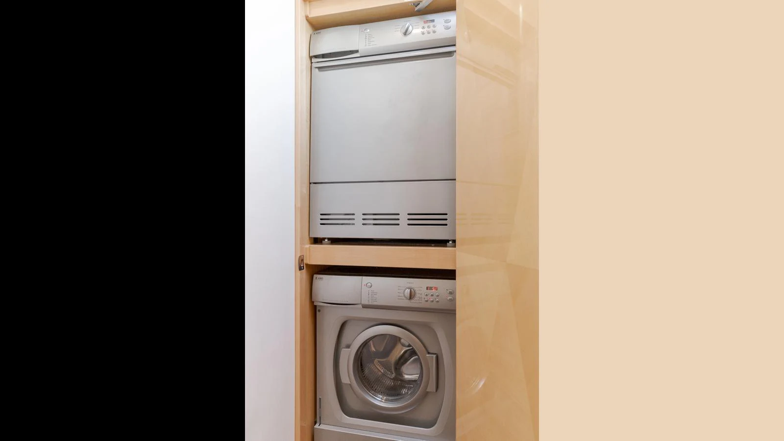 The image shows a compact laundry area with a stacked washer and dryer unit. aboard SEAQUEL Yacht for Sale