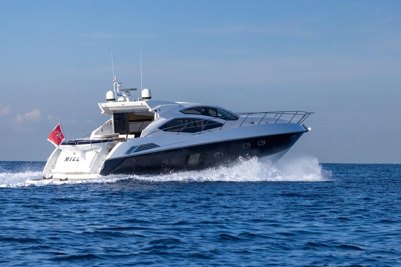 A sleek yacht cruises swiftly over calm blue waters under a clear sky. aboard M/Y MIEL Yacht for Sale