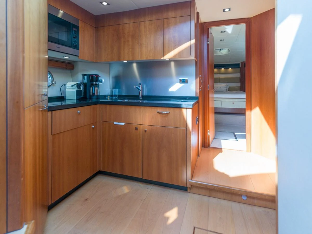 The yacht's galley features sleek wooden cabinetry and modern appliances, leading into a cozy stateroom. aboard M/Y MIEL Yacht for Sale
