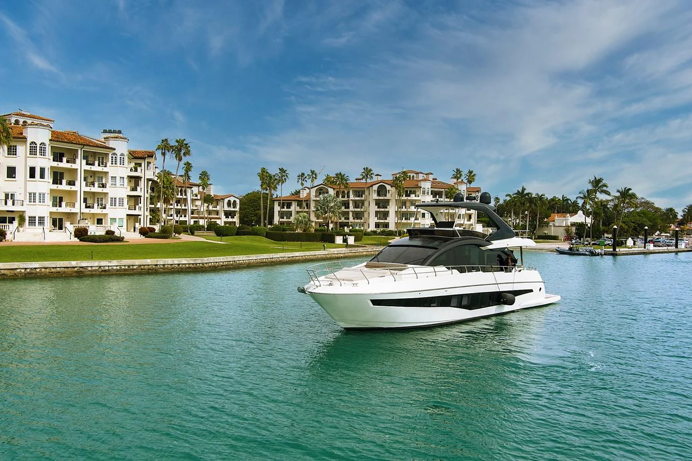 A sleek yacht cruises through serene waters with a backdrop of luxurious waterfront residences. aboard JESSEA Yacht for Sale