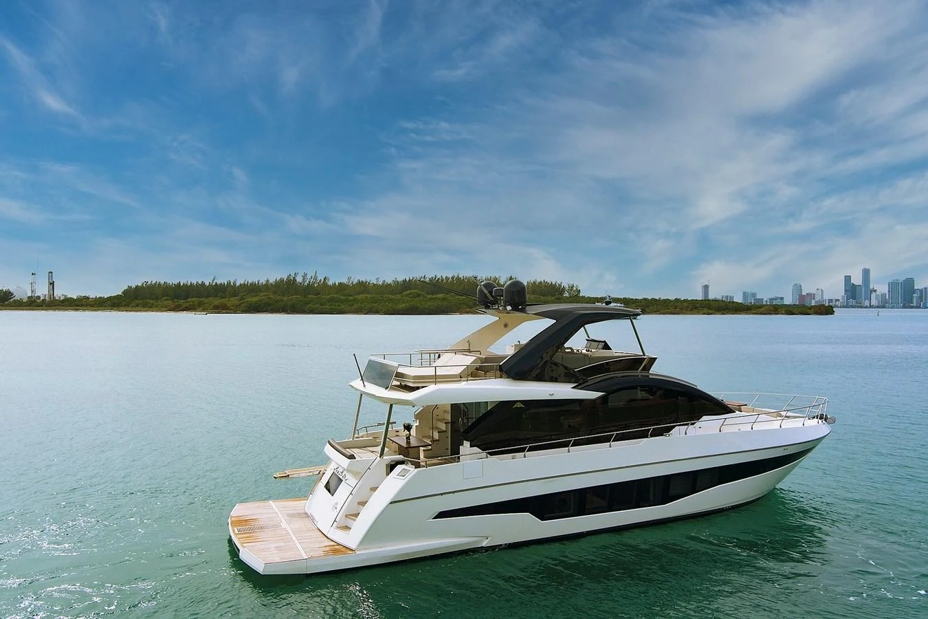 A sleek and modern yacht cruising on calm waters with a city skyline in the background. aboard JESSEA Yacht for Sale
