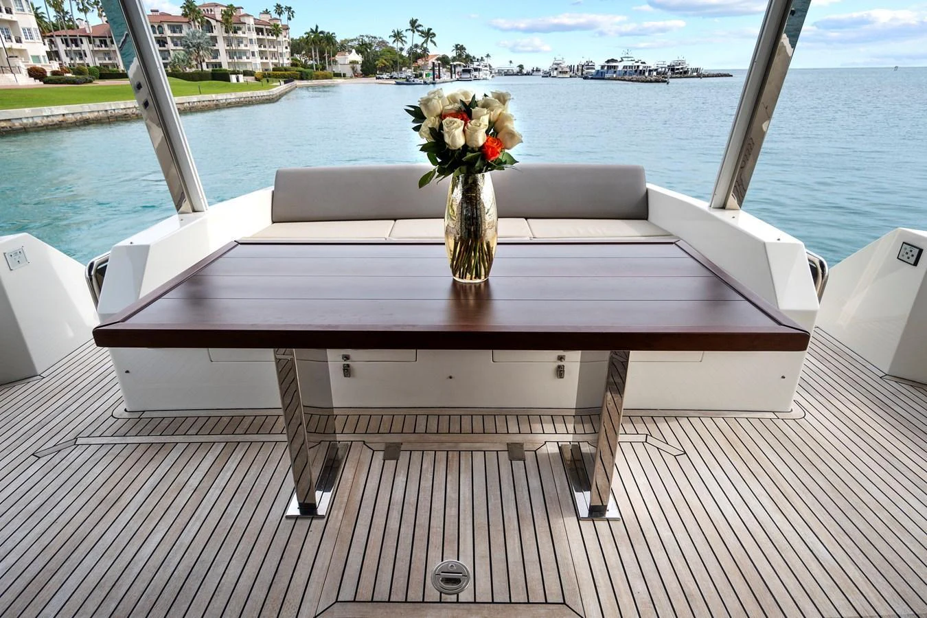 The aft deck features a stylish wooden table with a floral centerpiece, offering a serene view of the water and nearby buildings. aboard JESSEA Yacht for Sale