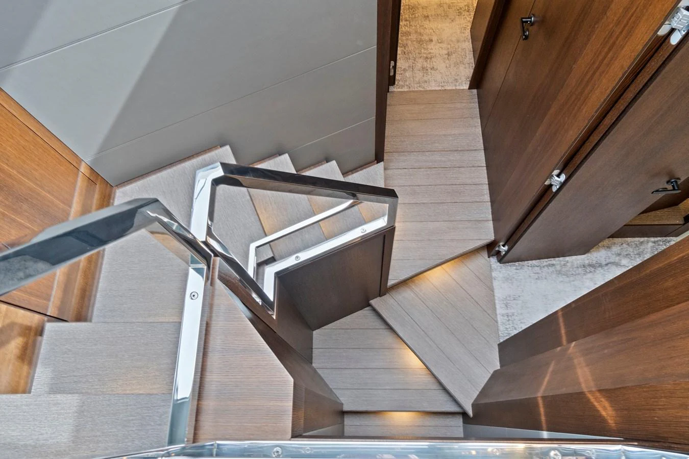 A modern staircase with sleek wooden steps and stainless steel handrails connects different levels of the yacht's interior. aboard JESSEA Yacht for Sale