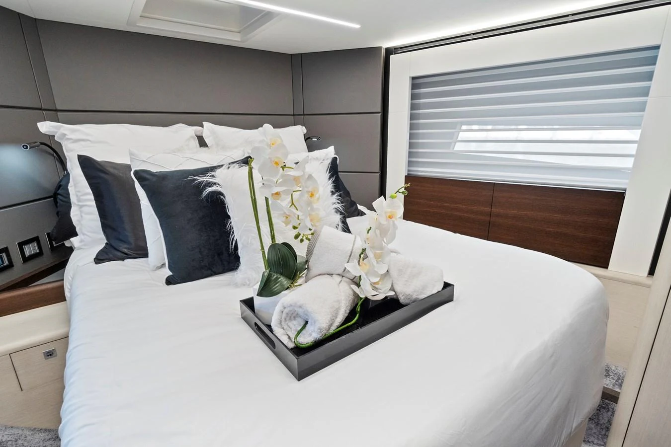 The stateroom features a luxurious bed adorned with plush pillows and a decorative tray with flowers. aboard JESSEA Yacht for Sale