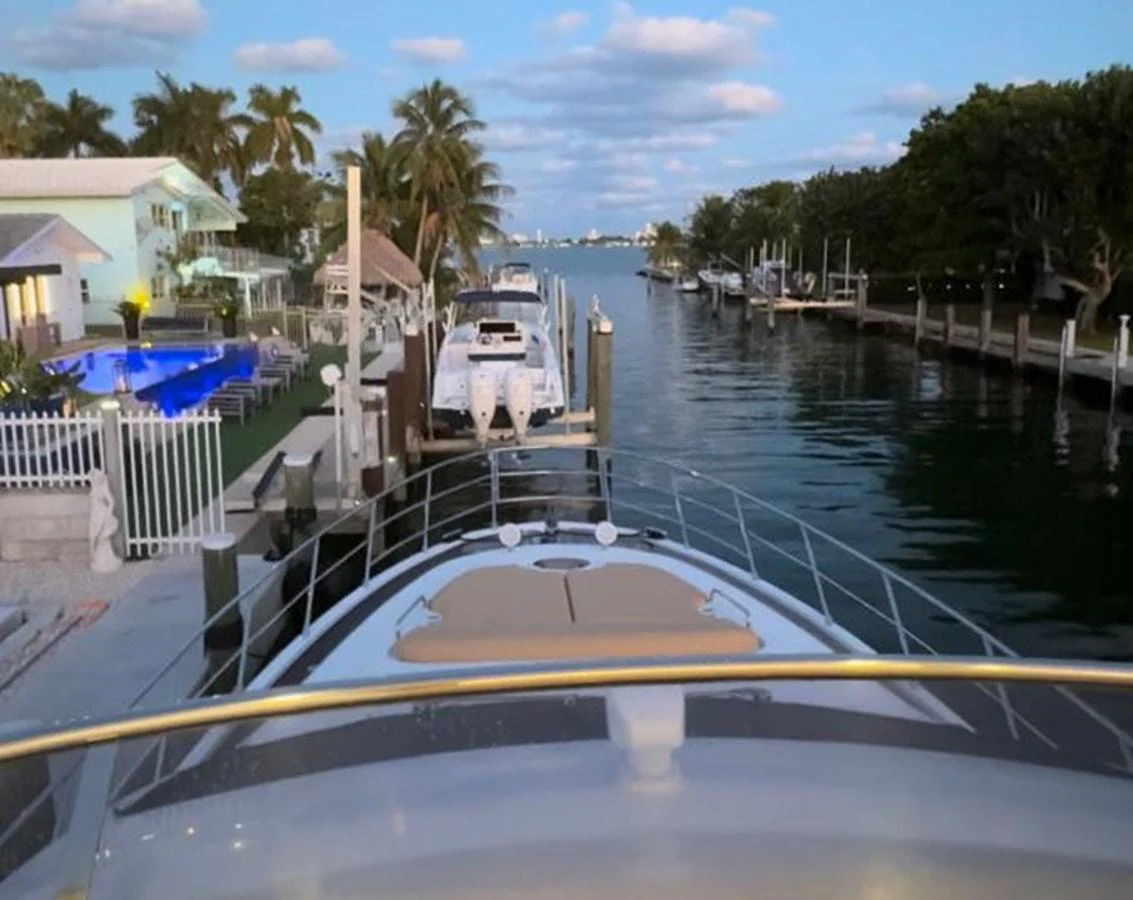 The yacht is docked in a serene canal, surrounded by lush greenery and waterfront homes. aboard TARKAN Yacht for Sale