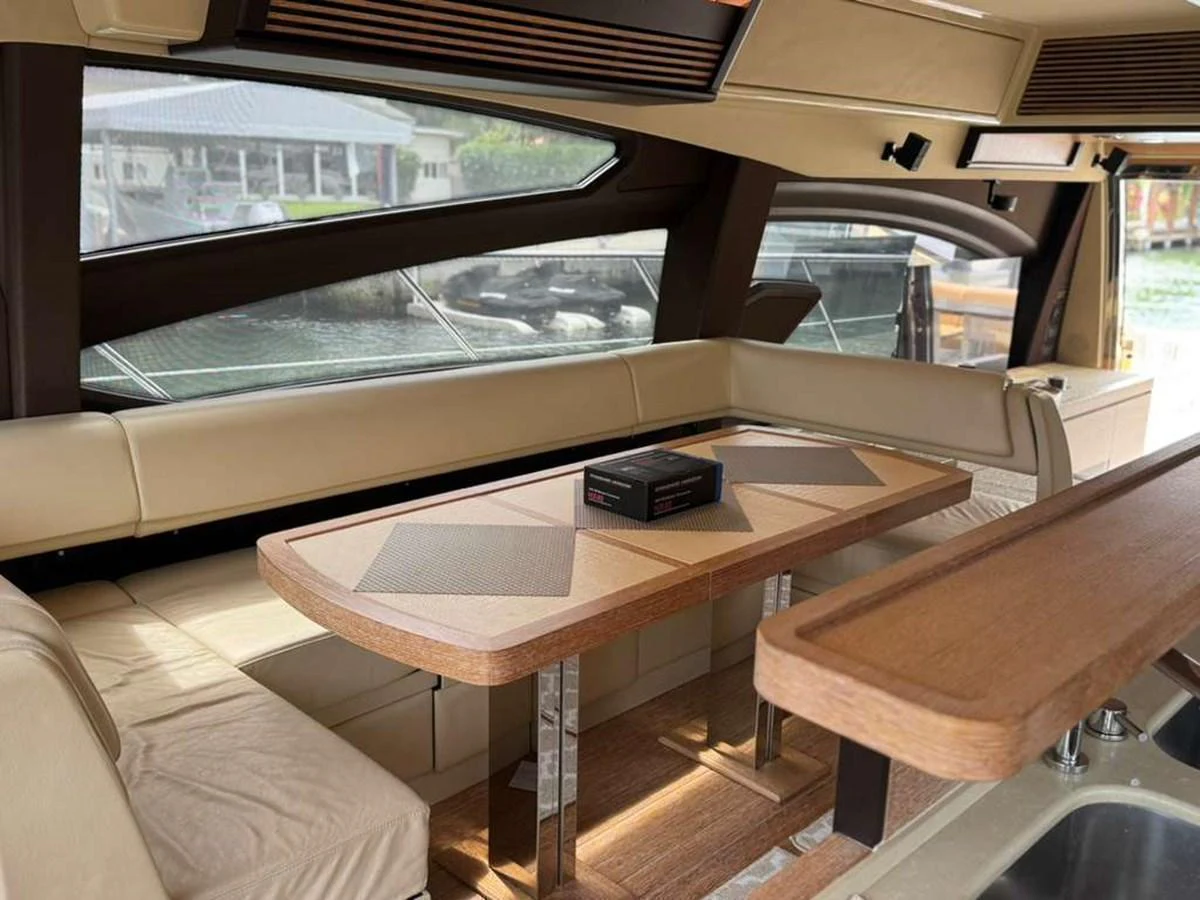 The saloon features a cozy seating area with a stylish wooden table and large windows offering a view of the marina. aboard TARKAN Yacht for Sale