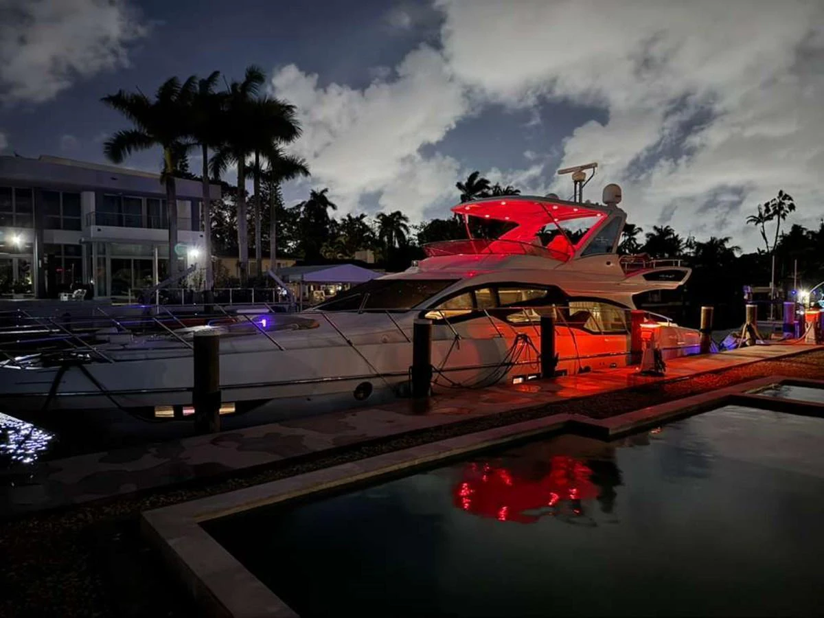 A sleek yacht is docked at night, illuminated by ambient lighting and surrounded by a serene marina setting. aboard TARKAN Yacht for Sale
