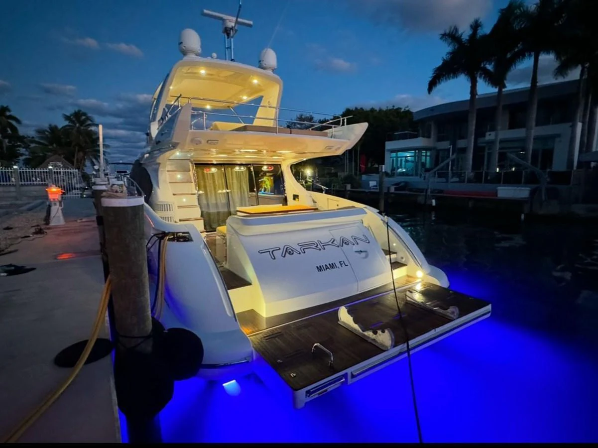 The yacht is docked at a marina, illuminated by vibrant blue underwater lights, creating a captivating evening ambiance. aboard TARKAN Yacht for Sale