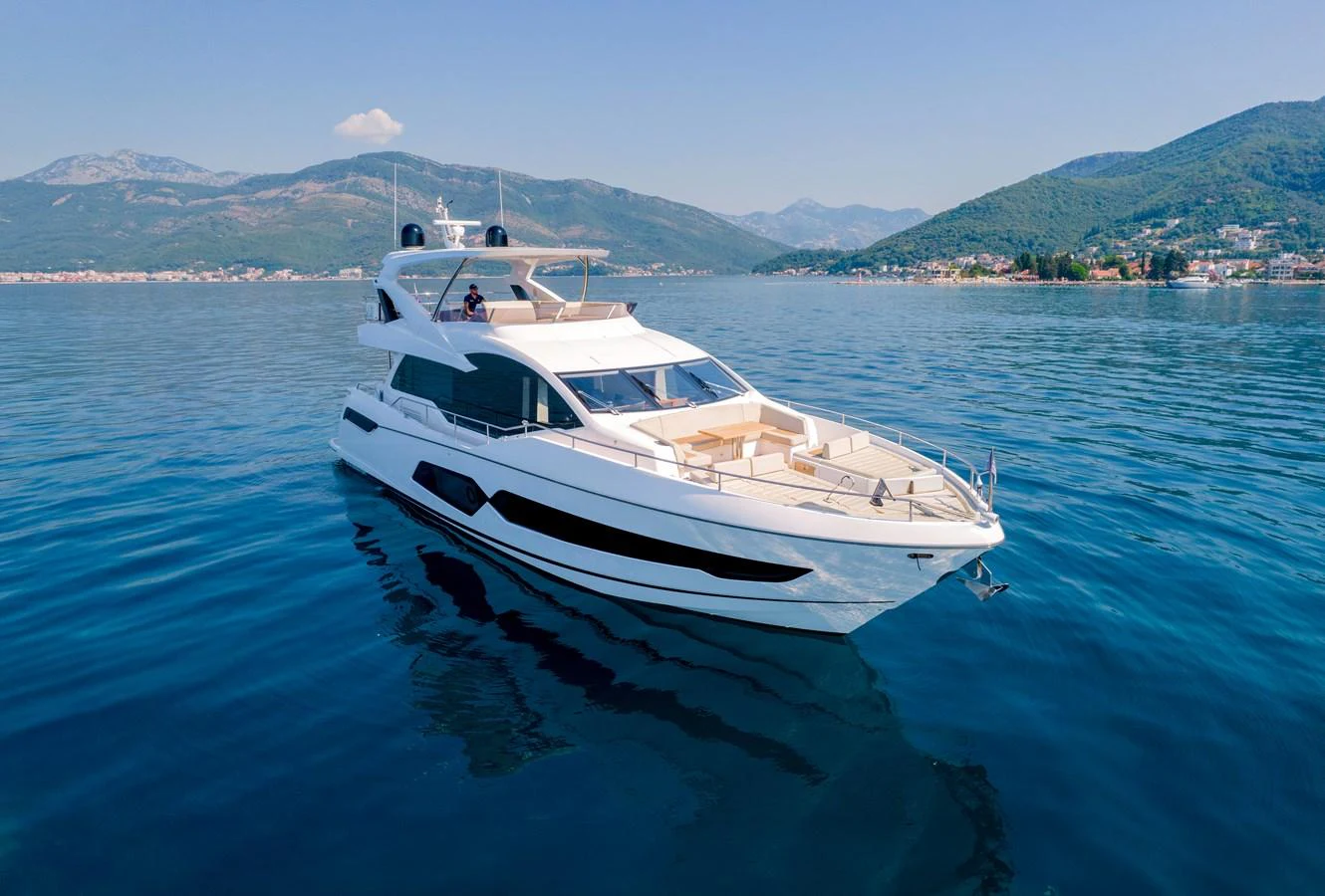 A sleek and modern yacht glides gracefully on calm waters with scenic mountains in the background. aboard SUNSEEKER 76Y Yacht for Sale