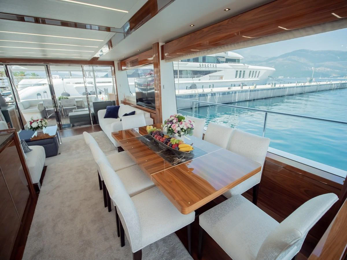 The yacht's dining area features a sleek wooden table with plush white chairs, offering a luxurious setting with a view of the marina. aboard SUNSEEKER 76Y Yacht for Sale
