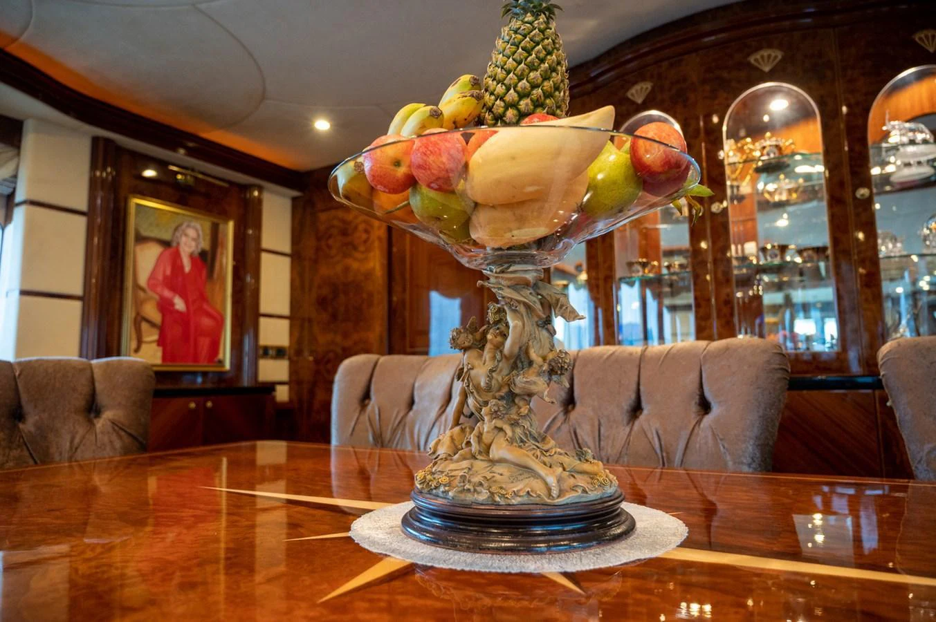 The yacht's dining area features an elegant table centerpiece with a fruit arrangement, surrounded by plush seating and rich wood finishes. aboard LADY EILEEN Yacht for Sale