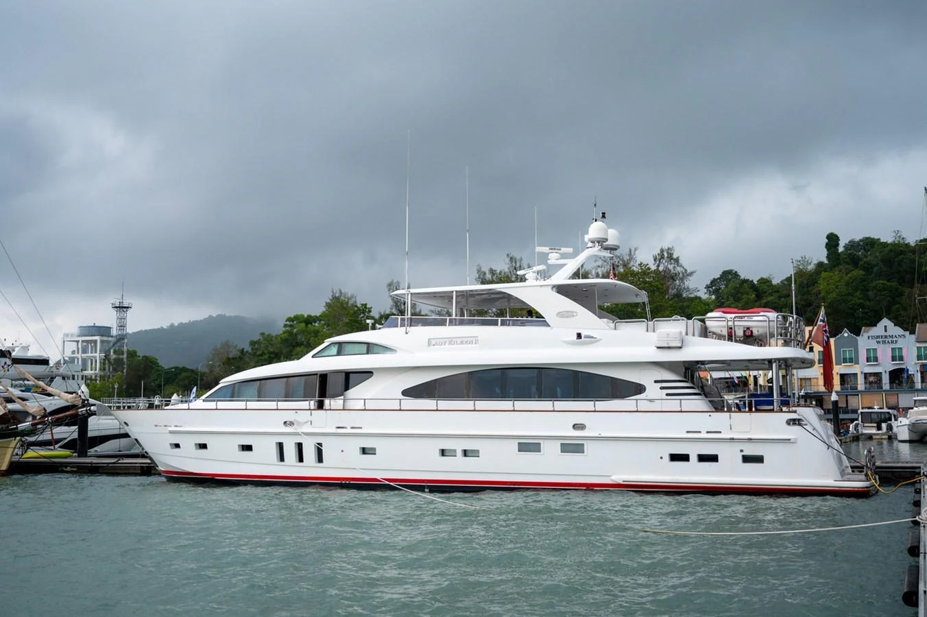 A sleek white yacht is docked at a marina under a cloudy sky. aboard LADY EILEEN Yacht for Sale