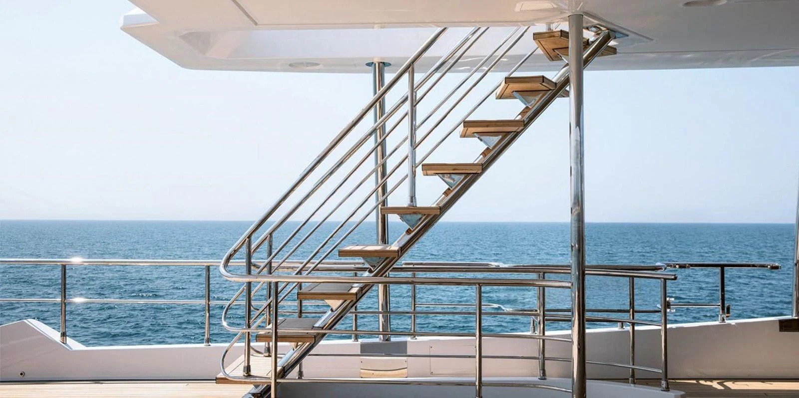 The aft deck features sleek, modern stairs leading to the upper deck with a stunning ocean view. aboard PANTERA Yacht for Sale