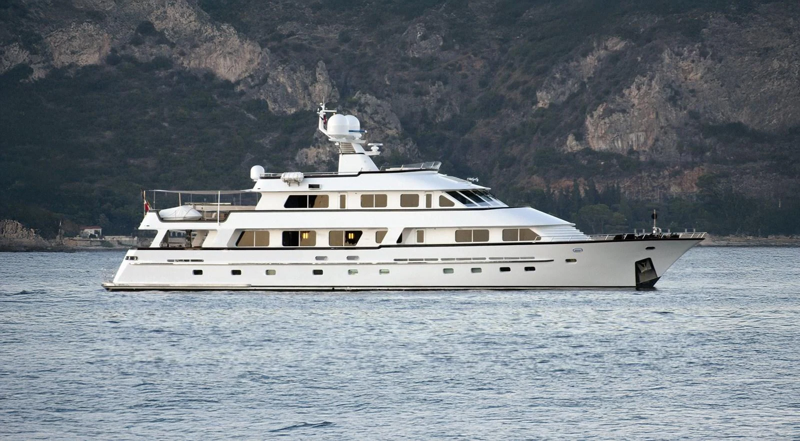 A sleek white yacht cruises gracefully on calm waters with a mountainous backdrop. aboard LIGAYA Yacht for Sale
