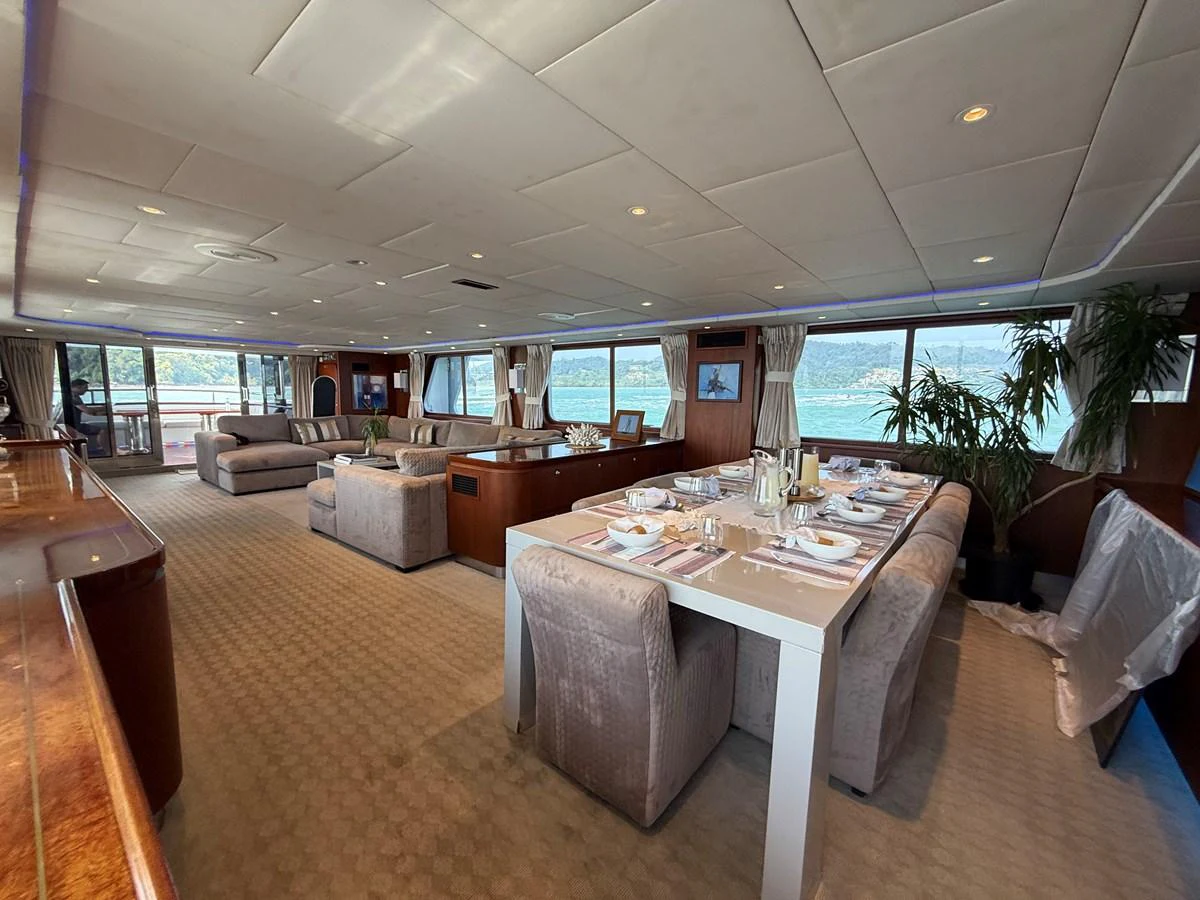The spacious salon features a comfortable seating area and a dining table with a scenic view. aboard LIGAYA Yacht for Sale