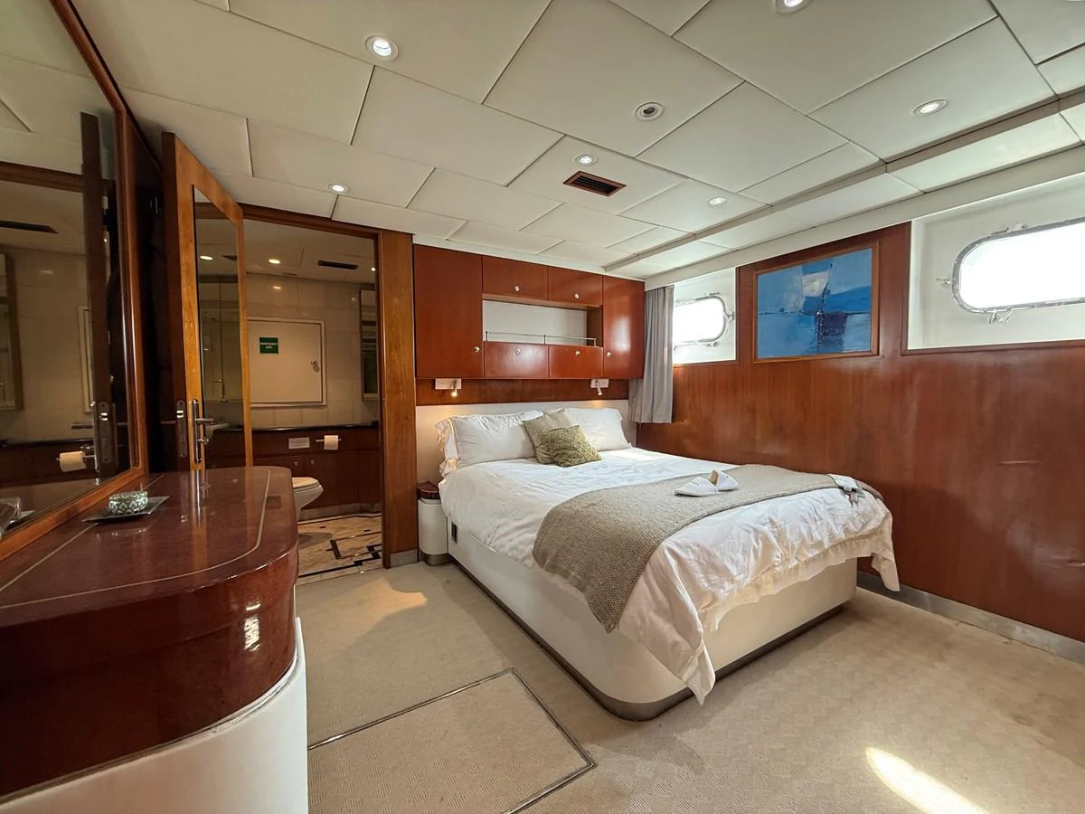 A luxurious stateroom featuring a comfortable bed, warm wood paneling, and ample natural light. aboard LIGAYA Yacht for Sale