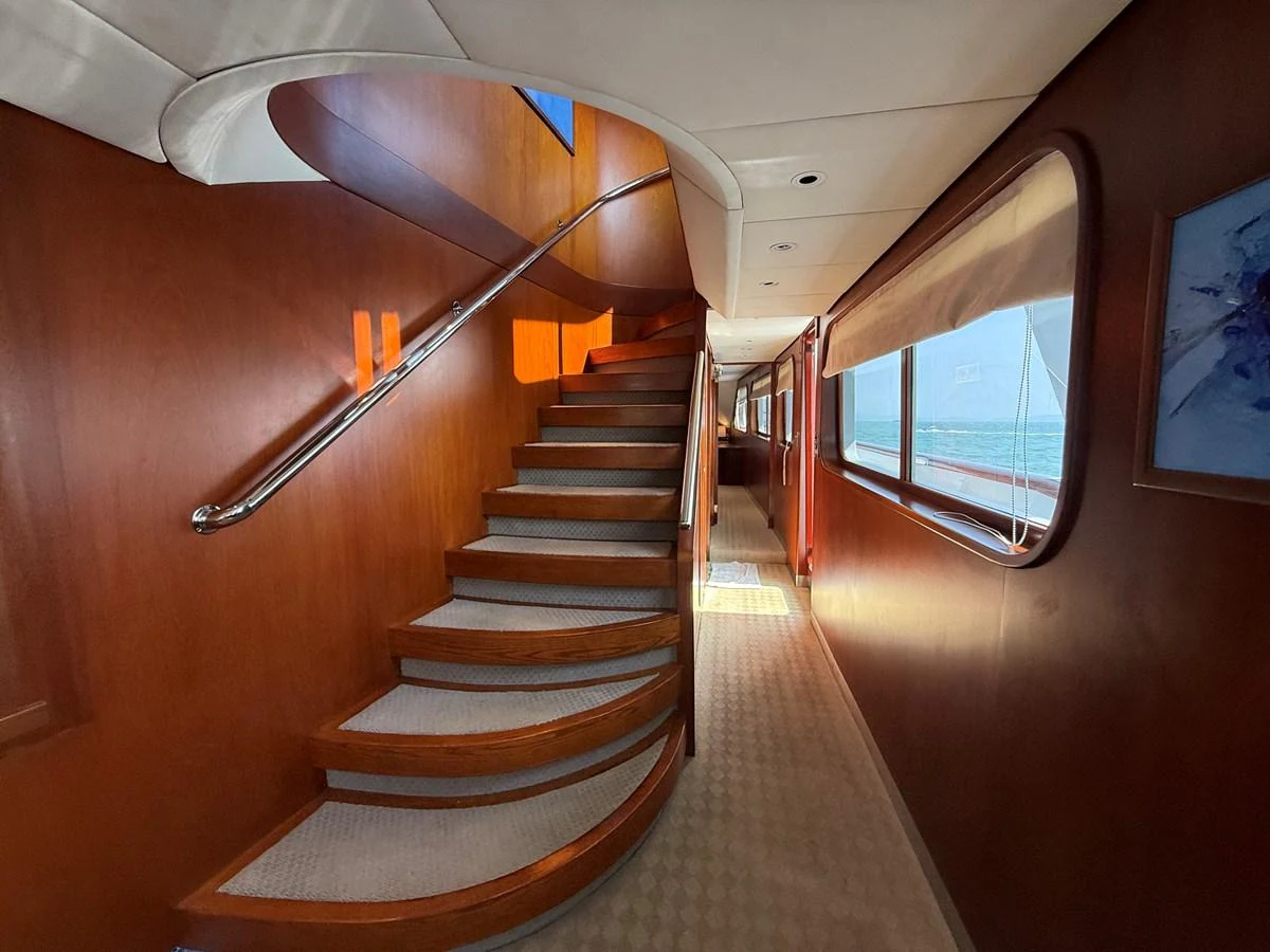 A beautifully crafted wooden staircase leads to the upper deck, illuminated by natural light streaming through the windows. aboard LIGAYA Yacht for Sale