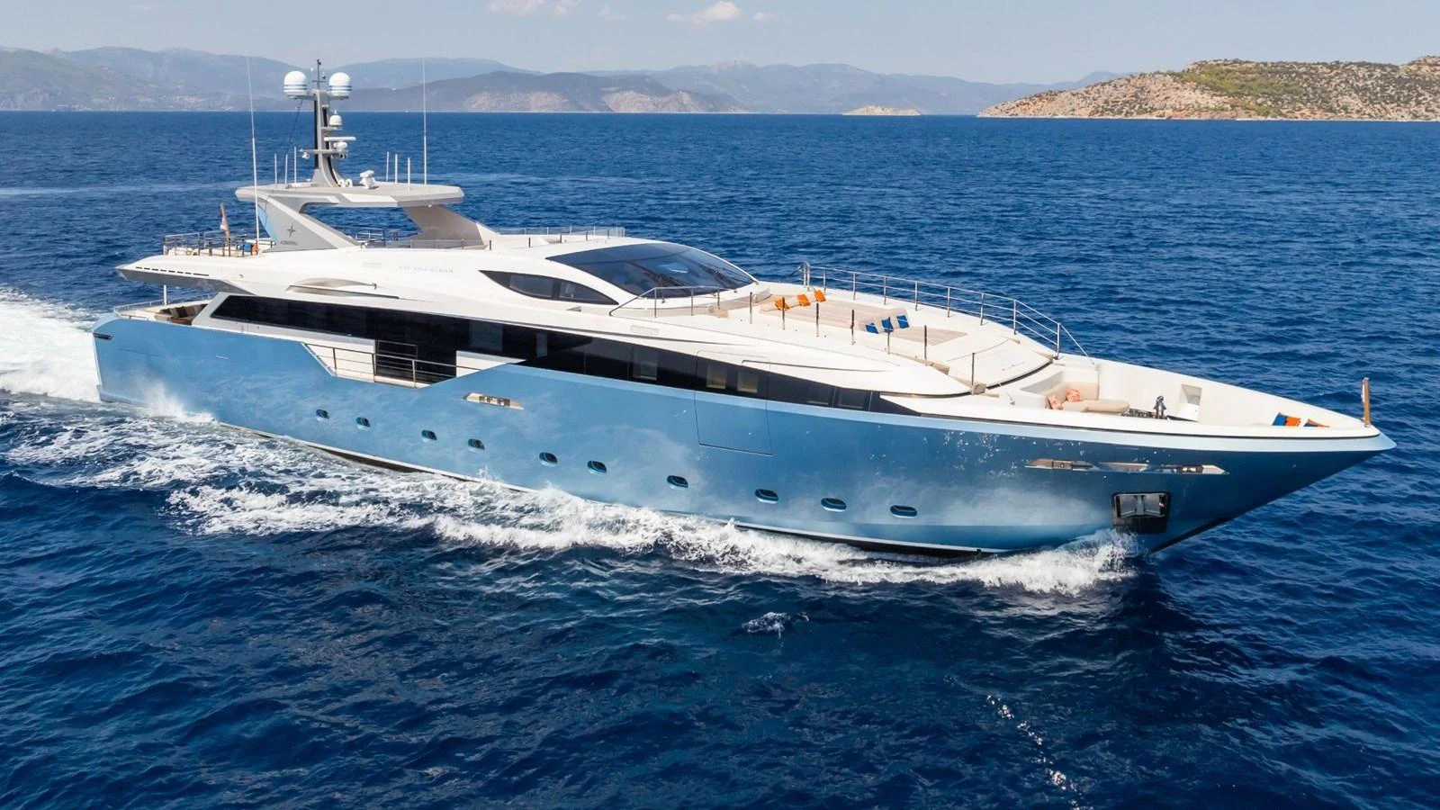 A sleek and modern yacht cruising through clear blue waters with a scenic coastline in the background. aboard BLUE MOON Yacht for Sale