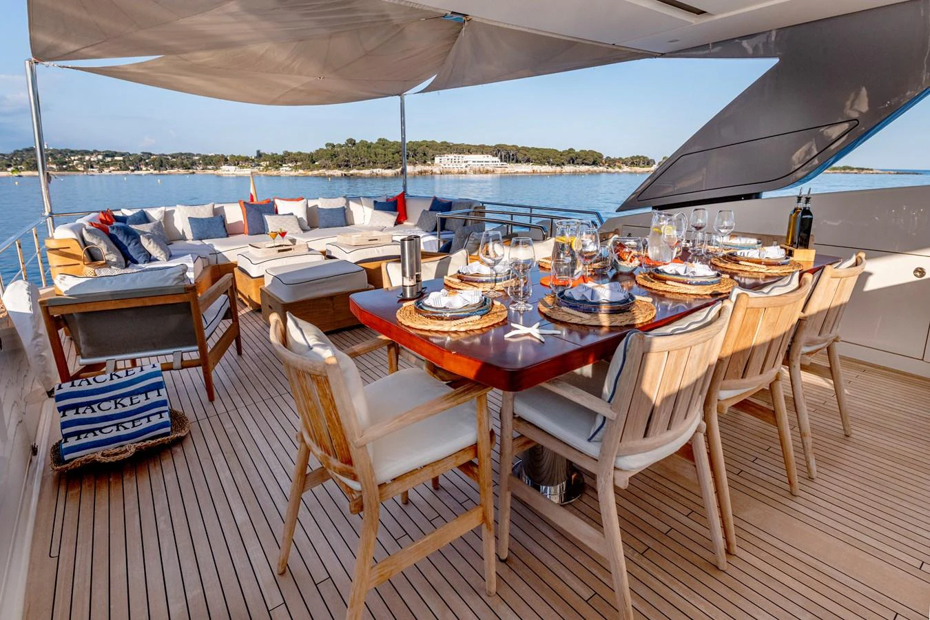 The aft deck offers an inviting dining area with a beautifully set table and a spacious lounging area overlooking serene waters. aboard CALM Yacht for Sale