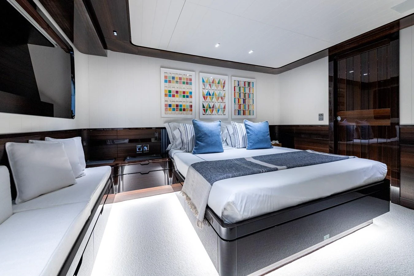 The stateroom features a modern design with a large bed, elegant wood finishes, and ambient lighting. aboard CALM Yacht for Sale