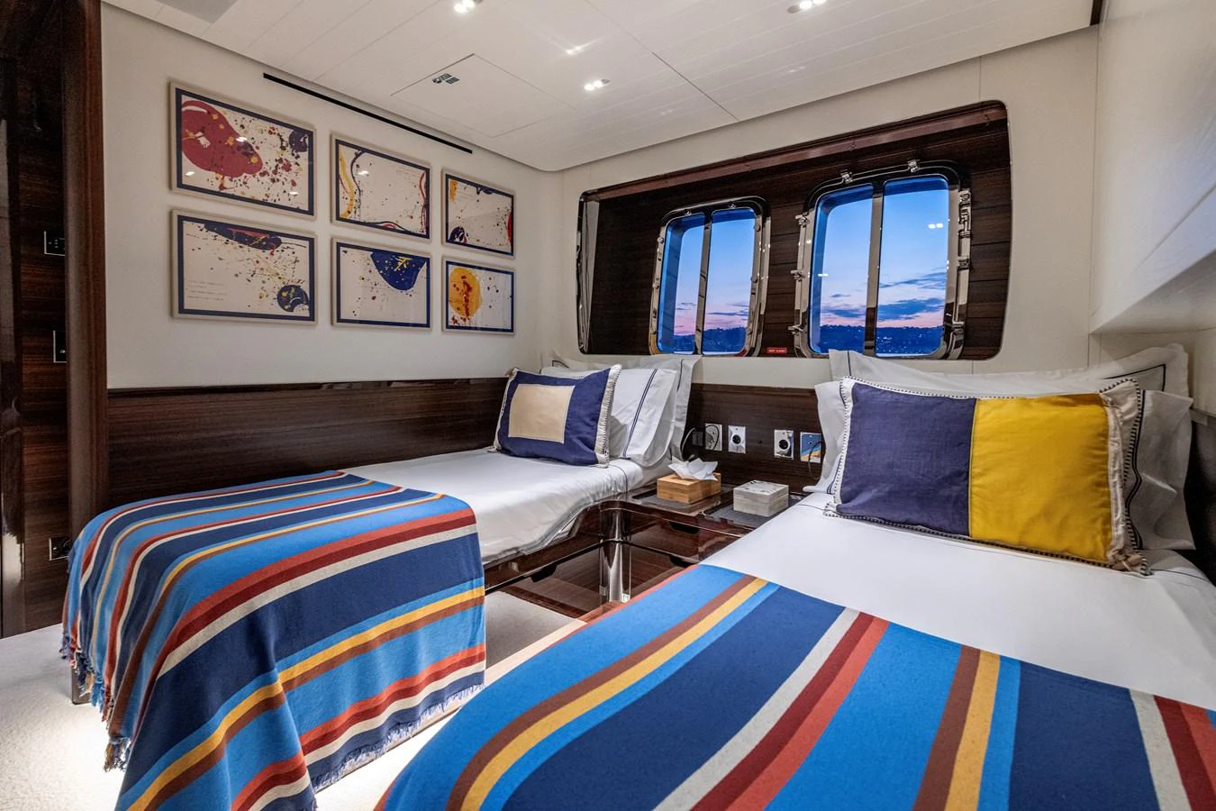 The guest stateroom features twin beds with colorful bedding and modern art on the walls, creating a cozy and inviting atmosphere. aboard CALM Yacht for Sale