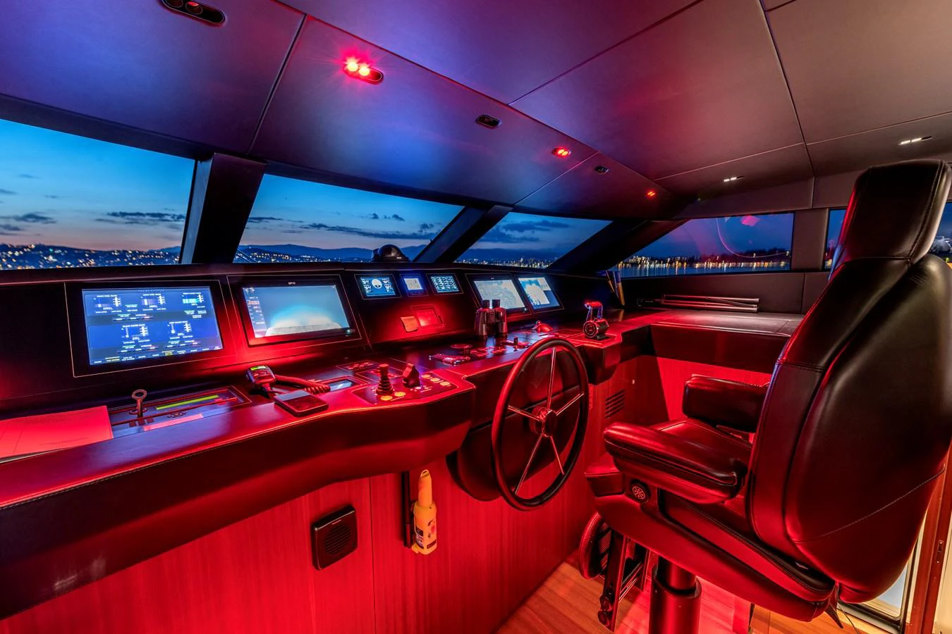 The helm station features advanced navigation equipment and a luxurious captain's chair, illuminated by ambient red lighting. aboard CALM Yacht for Sale