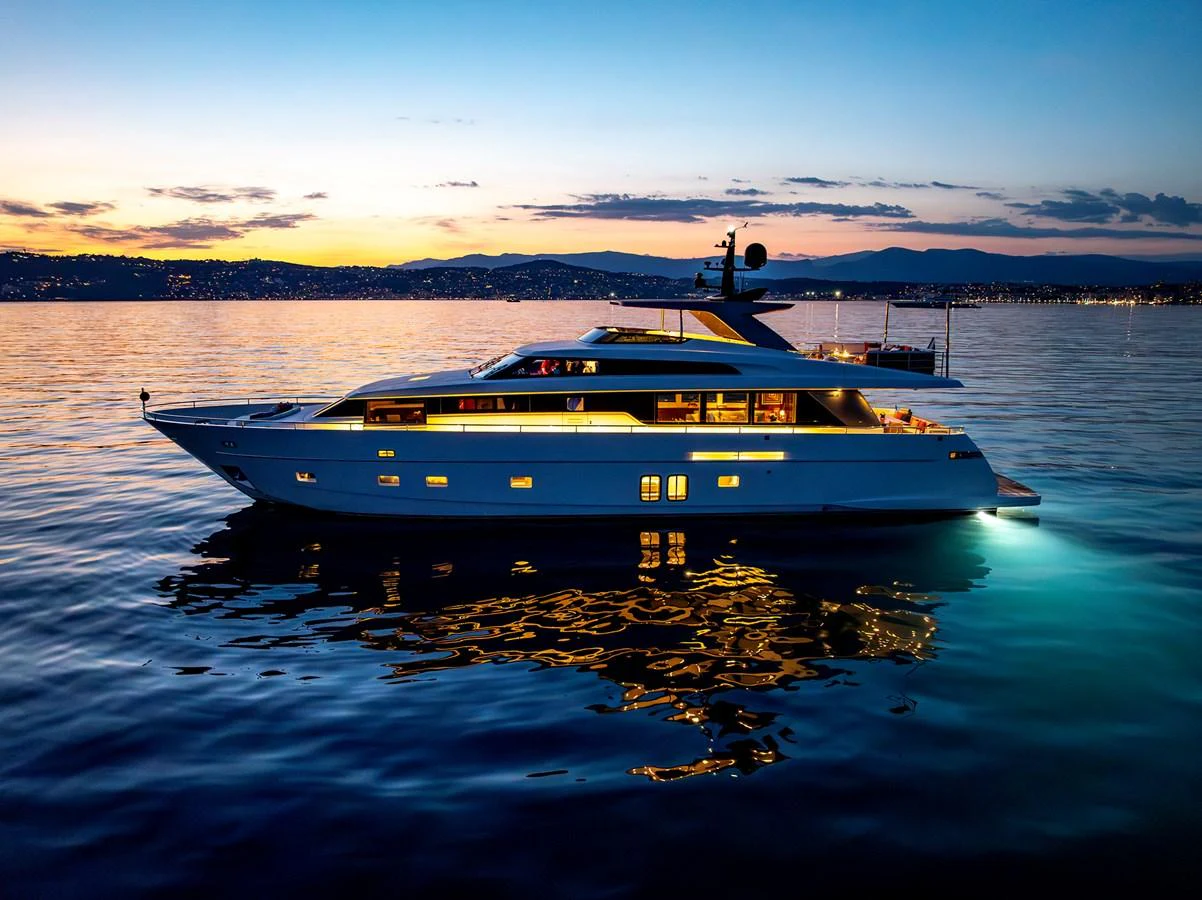 A sleek and modern yacht is illuminated against a serene evening backdrop on the water. aboard CALM Yacht for Sale