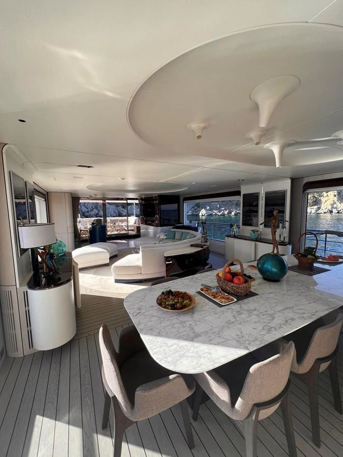 The yacht's salon features a stylish dining area with a marble table and comfortable seating, complemented by panoramic windows offering stunning views. aboard DAGUSHA V Yacht for Sale