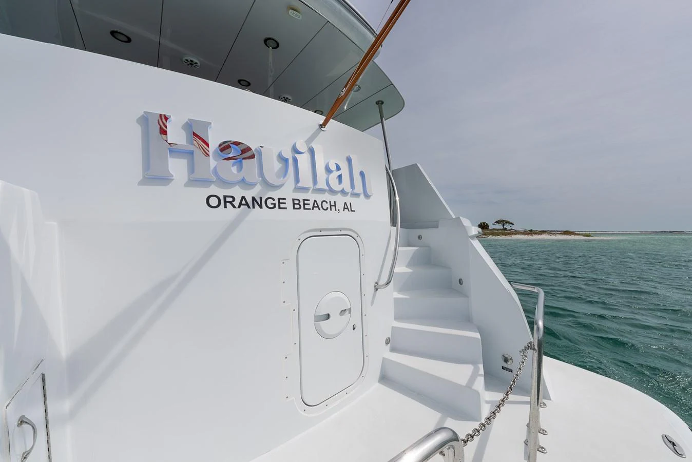 The yacht's aft deck features a sleek staircase leading to the upper deck, with a serene ocean backdrop. aboard HAVILAH Yacht for Sale