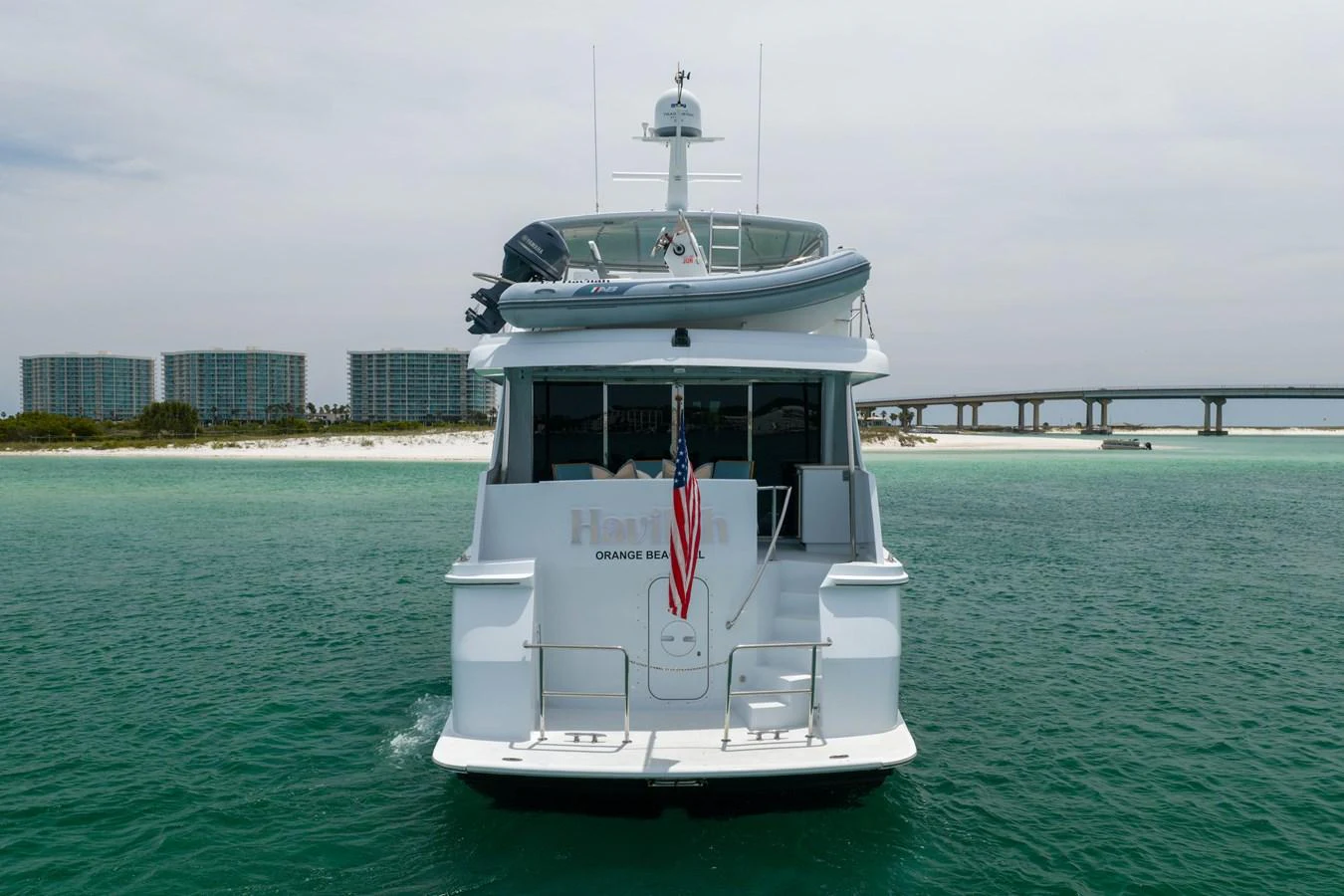 A yacht is seen from the rear, cruising on calm waters with a tender on the upper deck. aboard HAVILAH Yacht for Sale