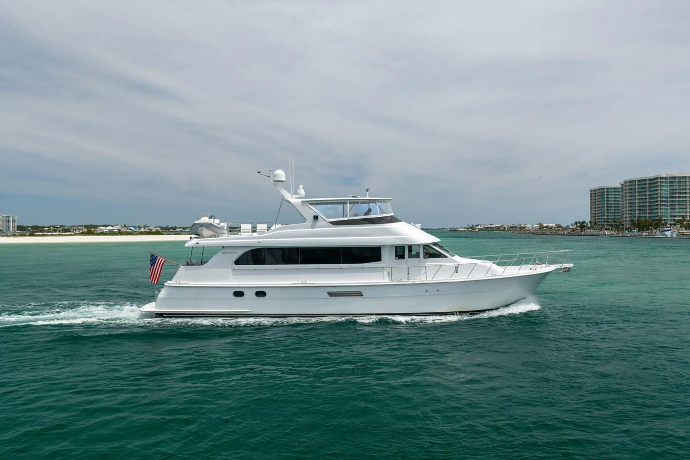 A sleek white yacht cruises through calm waters near a coastal city. aboard HAVILAH Yacht for Sale