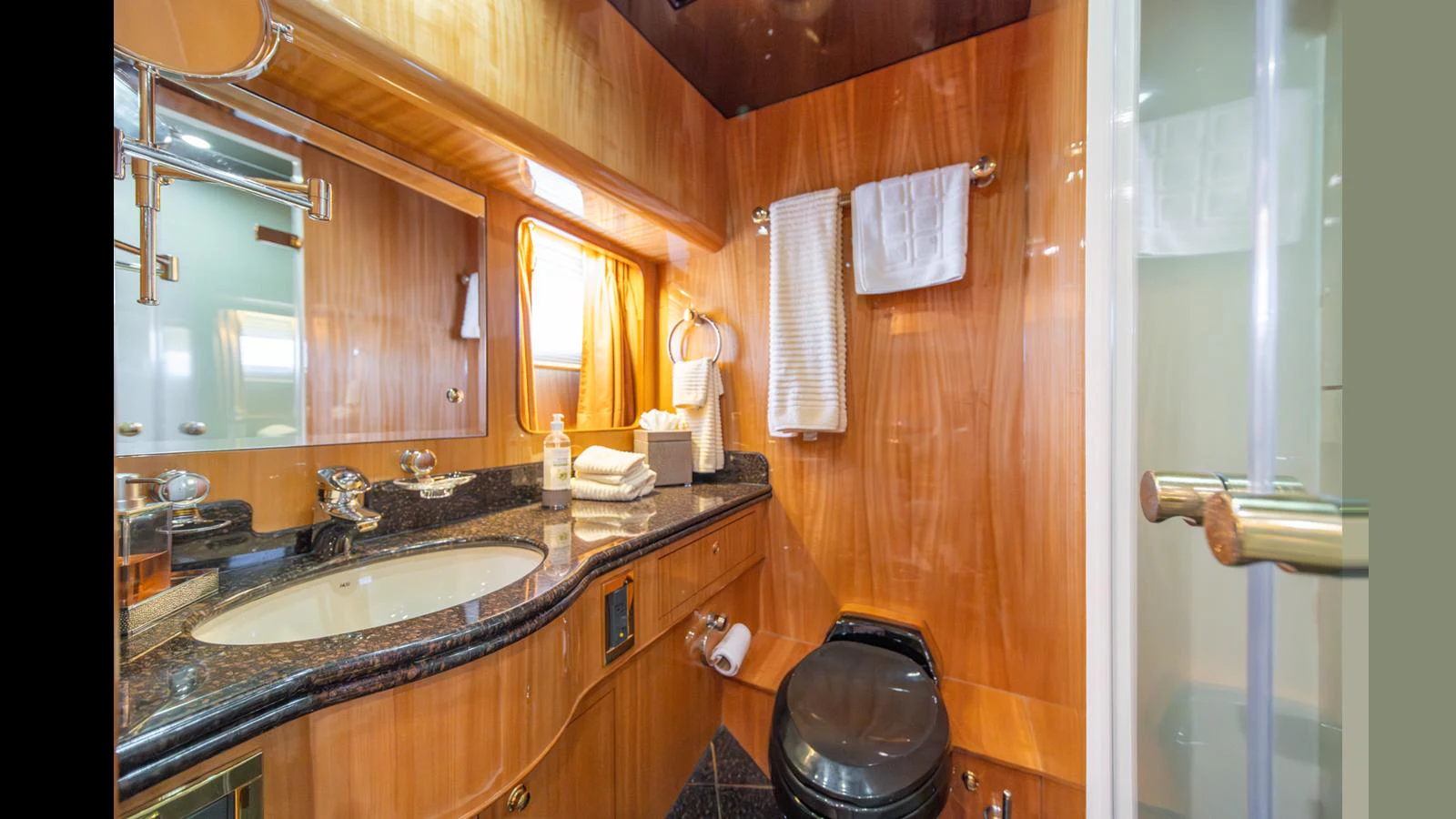The yacht's bathroom features elegant wood paneling, a sleek black countertop, and modern fixtures. aboard WISHES GRANTED Yacht for Sale