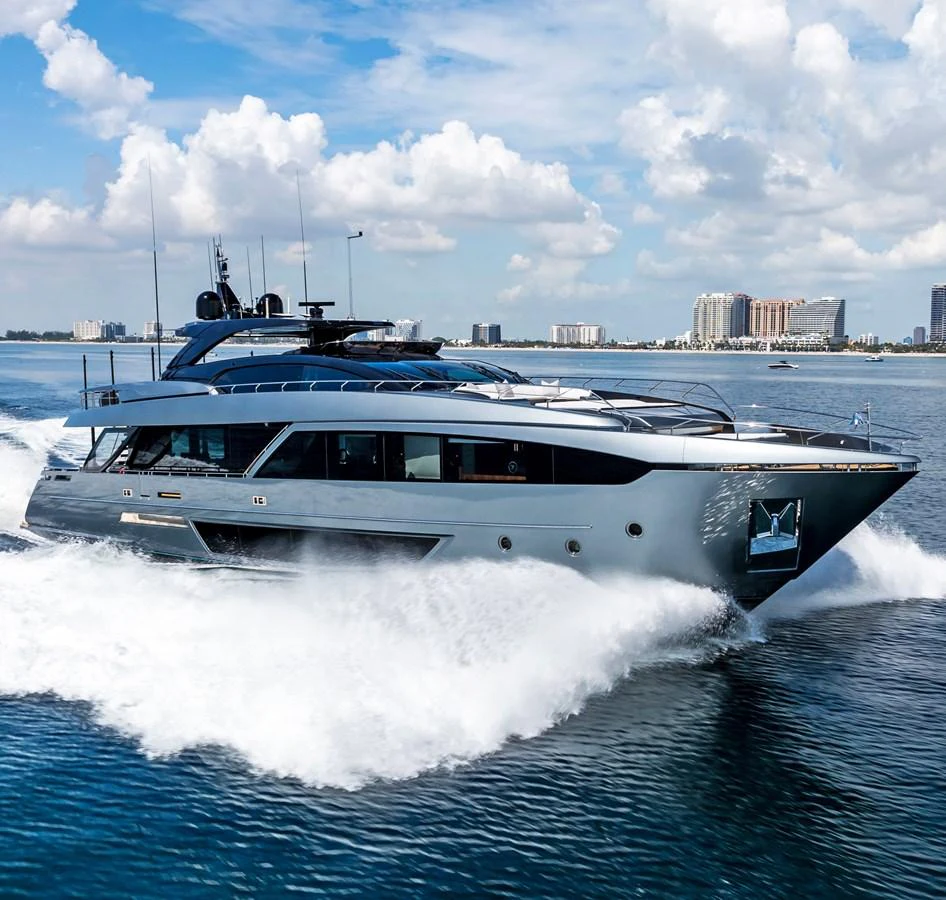 A sleek and modern yacht cruises swiftly through the water with a cityscape in the background. aboard NO SURRENDER Yacht for Sale