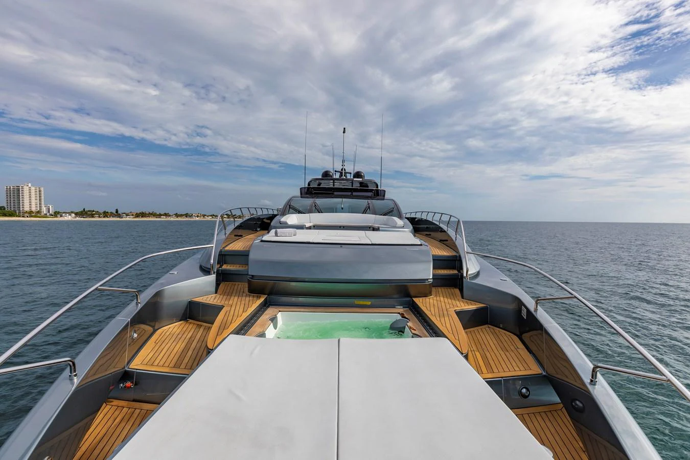 A sleek yacht with a spacious deck and modern design, cruising on calm waters under a partly cloudy sky. aboard NO SURRENDER Yacht for Sale