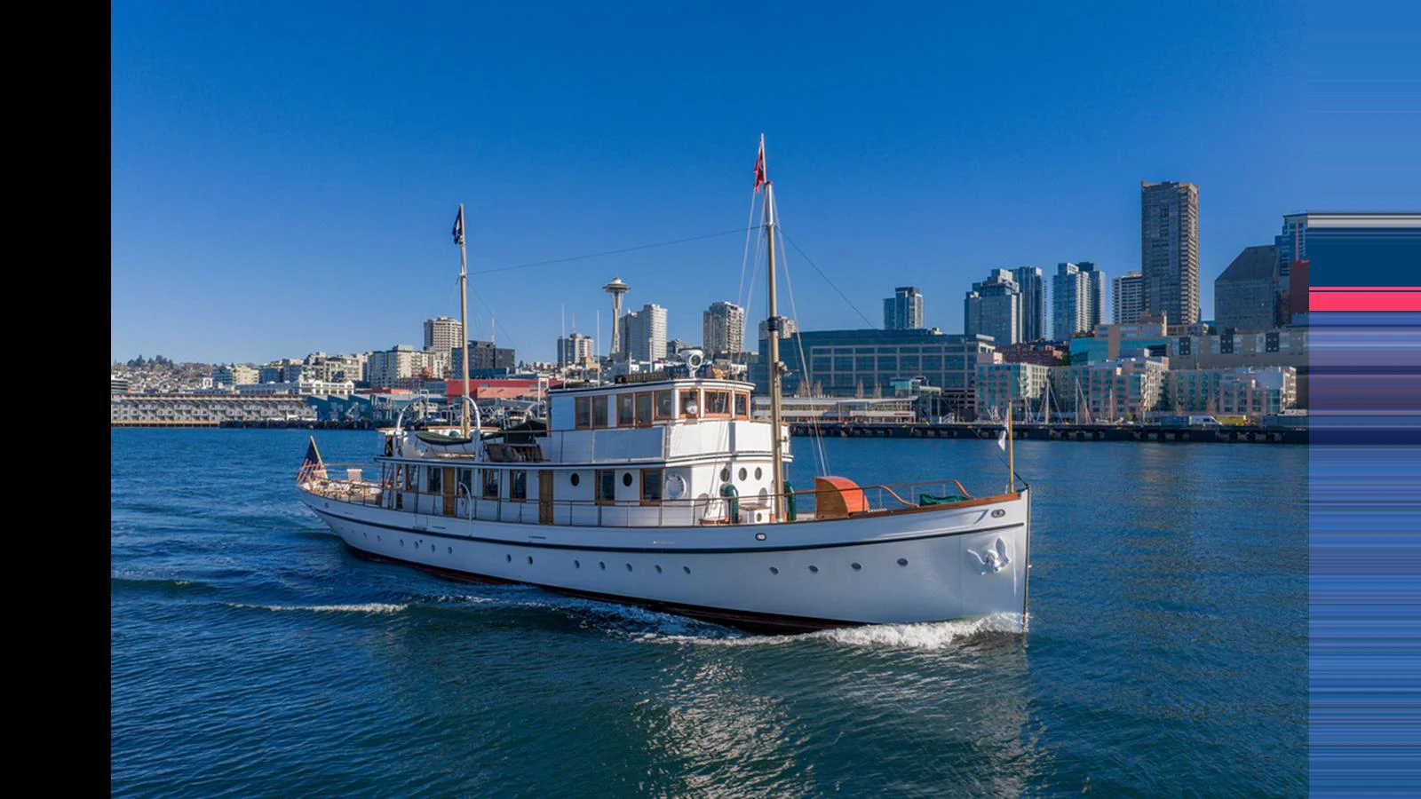 A classic yacht cruises through a vibrant city waterfront under a clear blue sky. aboard BLUE PETER Yacht for Sale