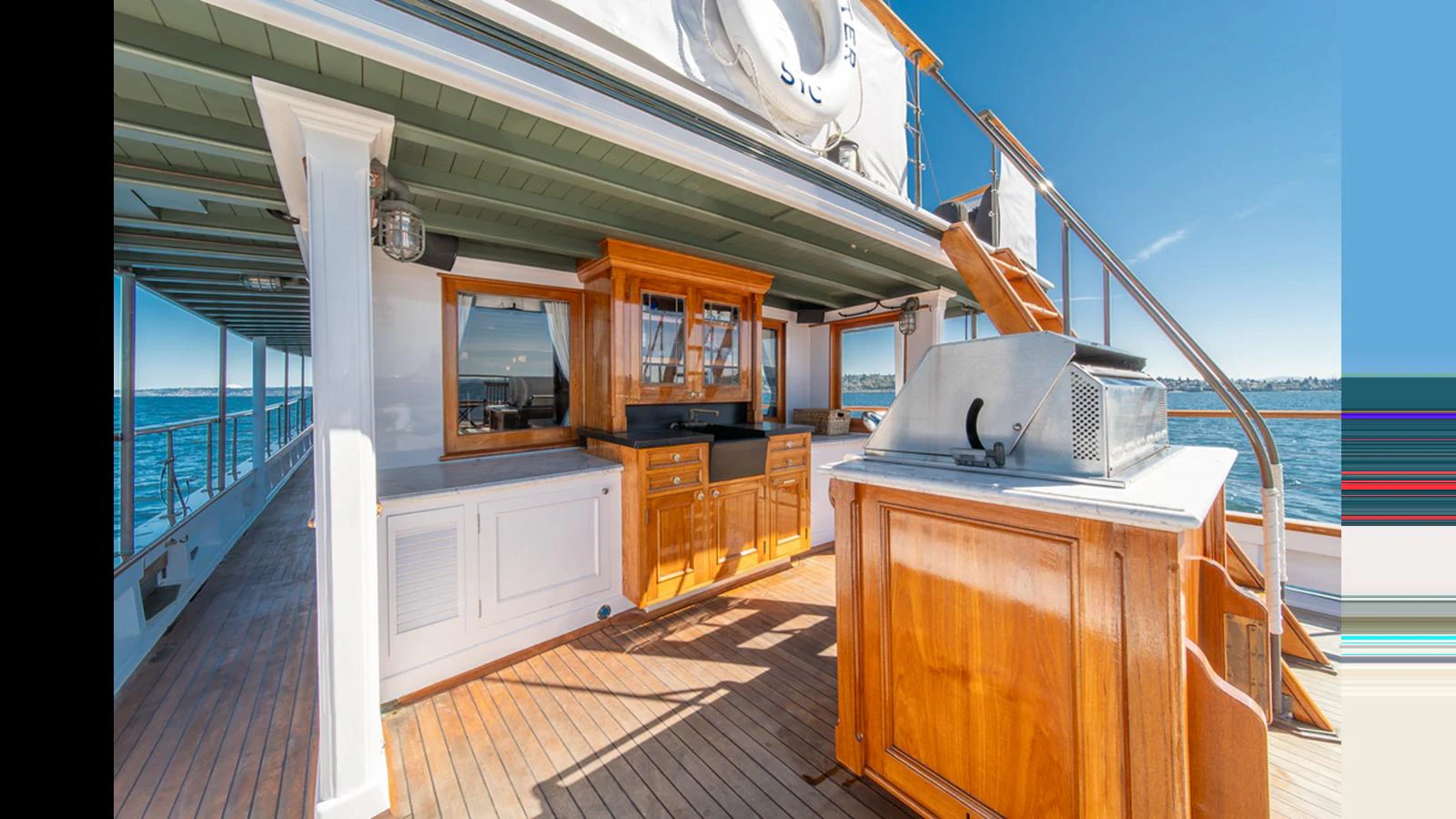 The aft deck features a well-appointed outdoor kitchen and dining area with beautiful wood finishes and a view of the sea. aboard BLUE PETER Yacht for Sale
