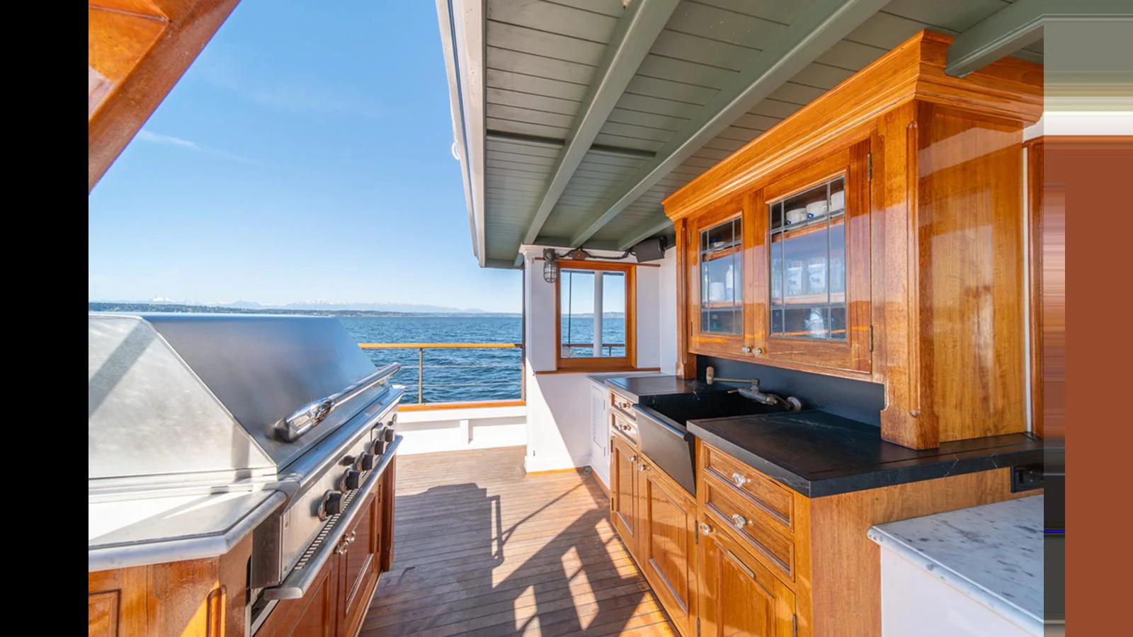 An inviting outdoor galley with a grill and wooden cabinetry, offering stunning sea views. aboard BLUE PETER Yacht for Sale
