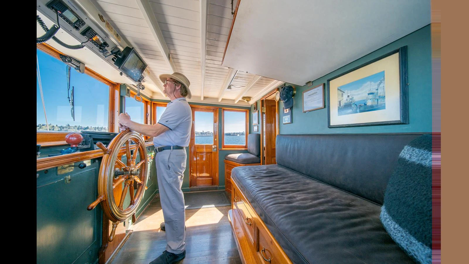 The helm area features a classic wooden steering wheel and a comfortable seating area with large windows providing ample natural light. aboard BLUE PETER Yacht for Sale