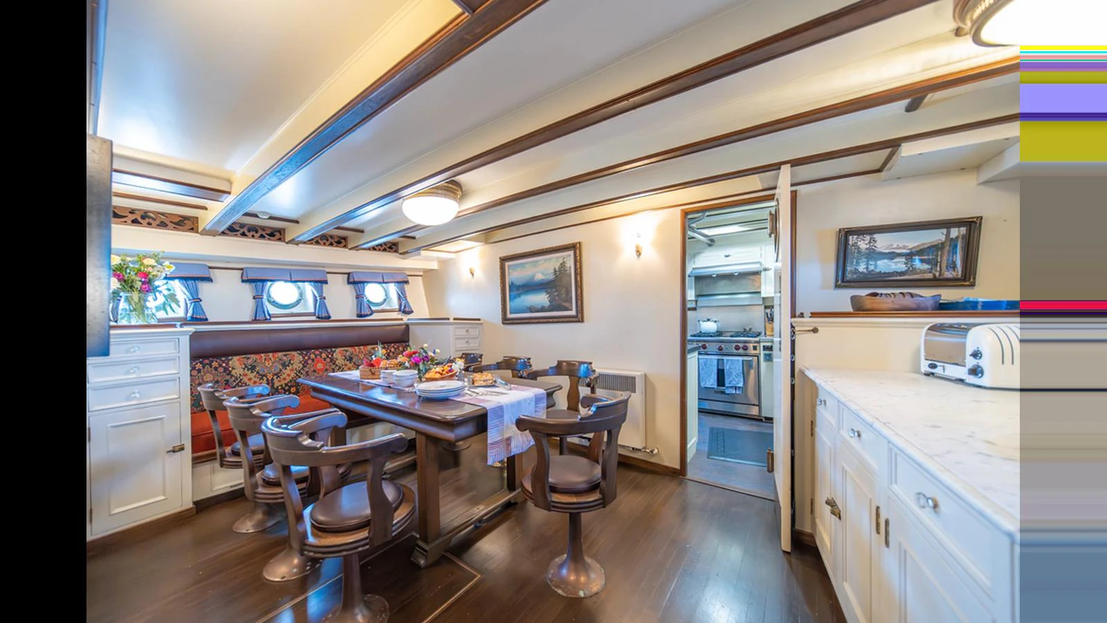 The yacht's dining area features a spacious table with elegant seating and a view into the galley. aboard BLUE PETER Yacht for Sale