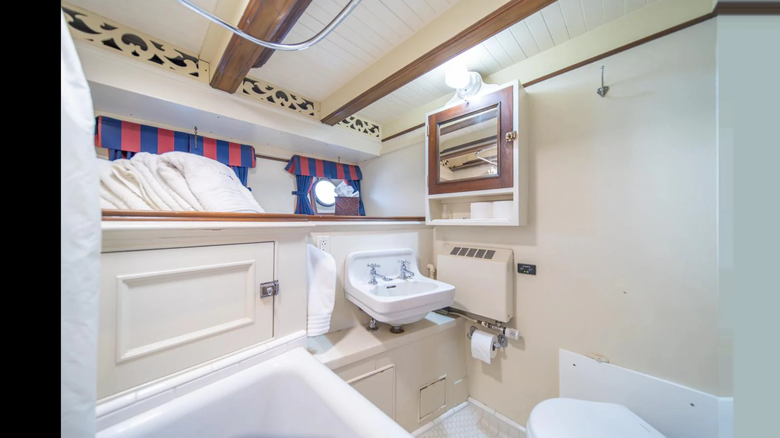 The yacht's bathroom features a classic design with a sink, mirror, and bathtub, complemented by nautical-themed curtains. aboard BLUE PETER Yacht for Sale