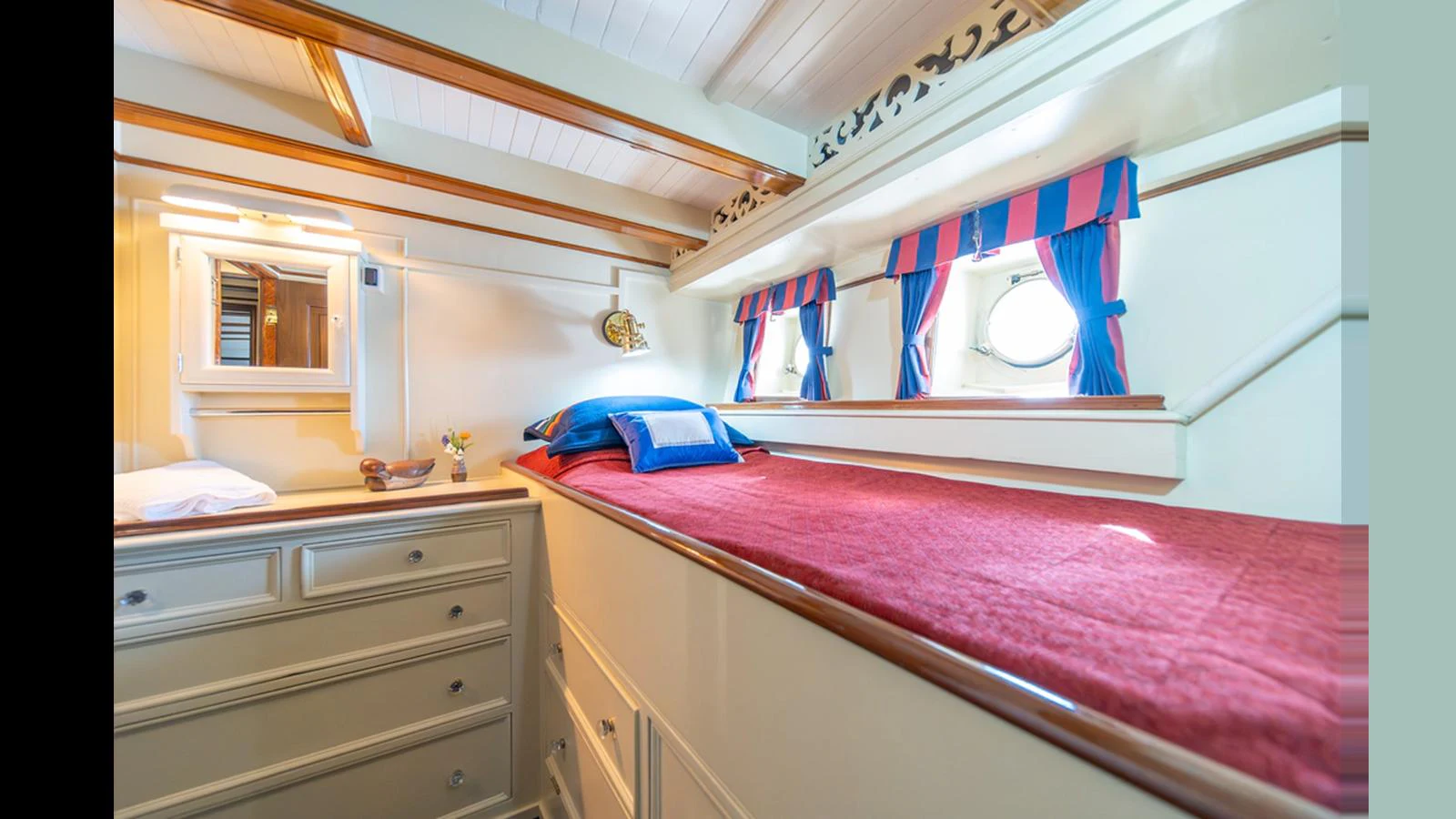 A cozy yacht cabin with a single bed, vibrant red bedding, and nautical-themed decor. aboard BLUE PETER Yacht for Sale