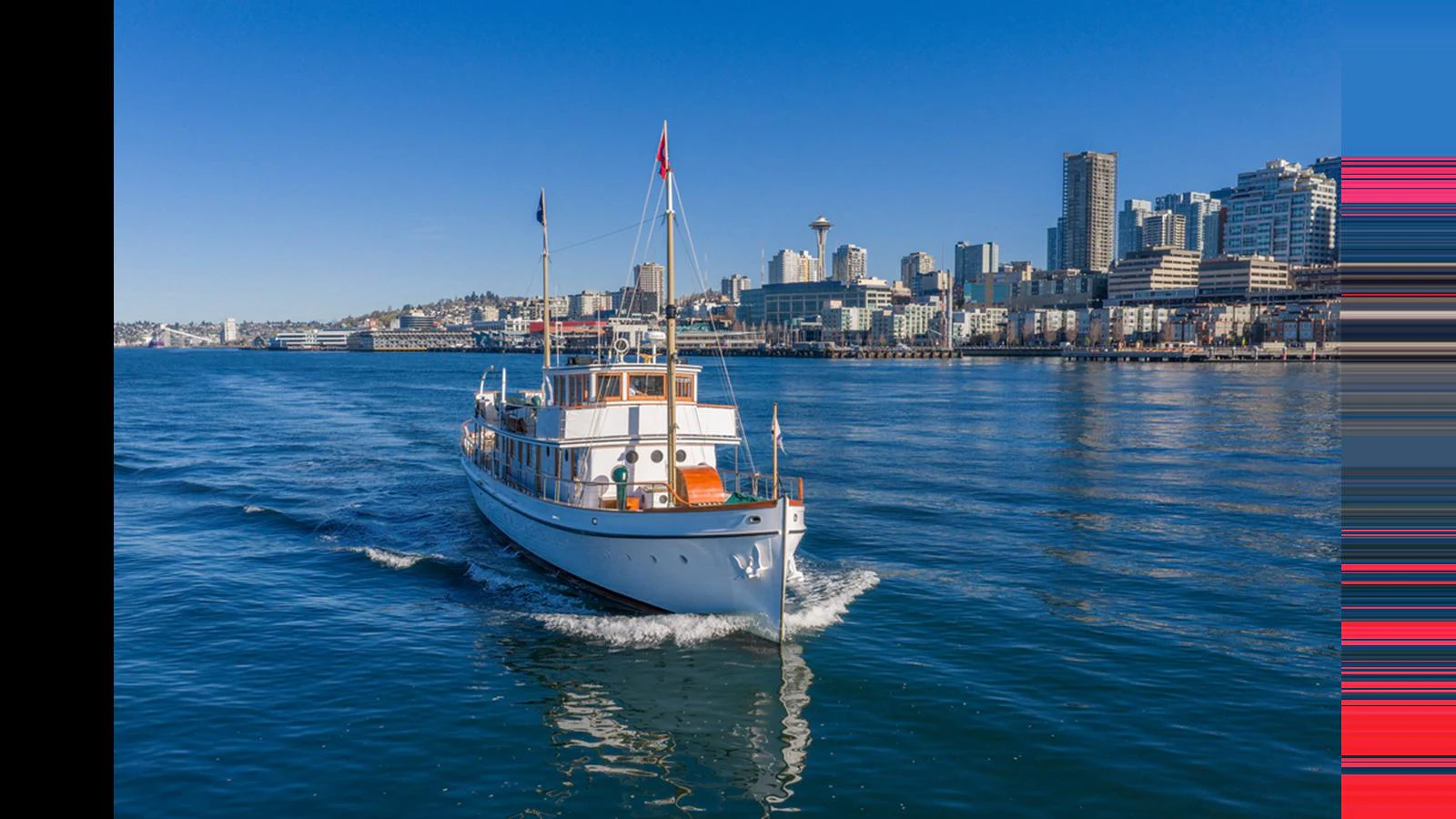 A classic yacht cruises gracefully on calm waters with a city skyline in the background. aboard BLUE PETER Yacht for Sale