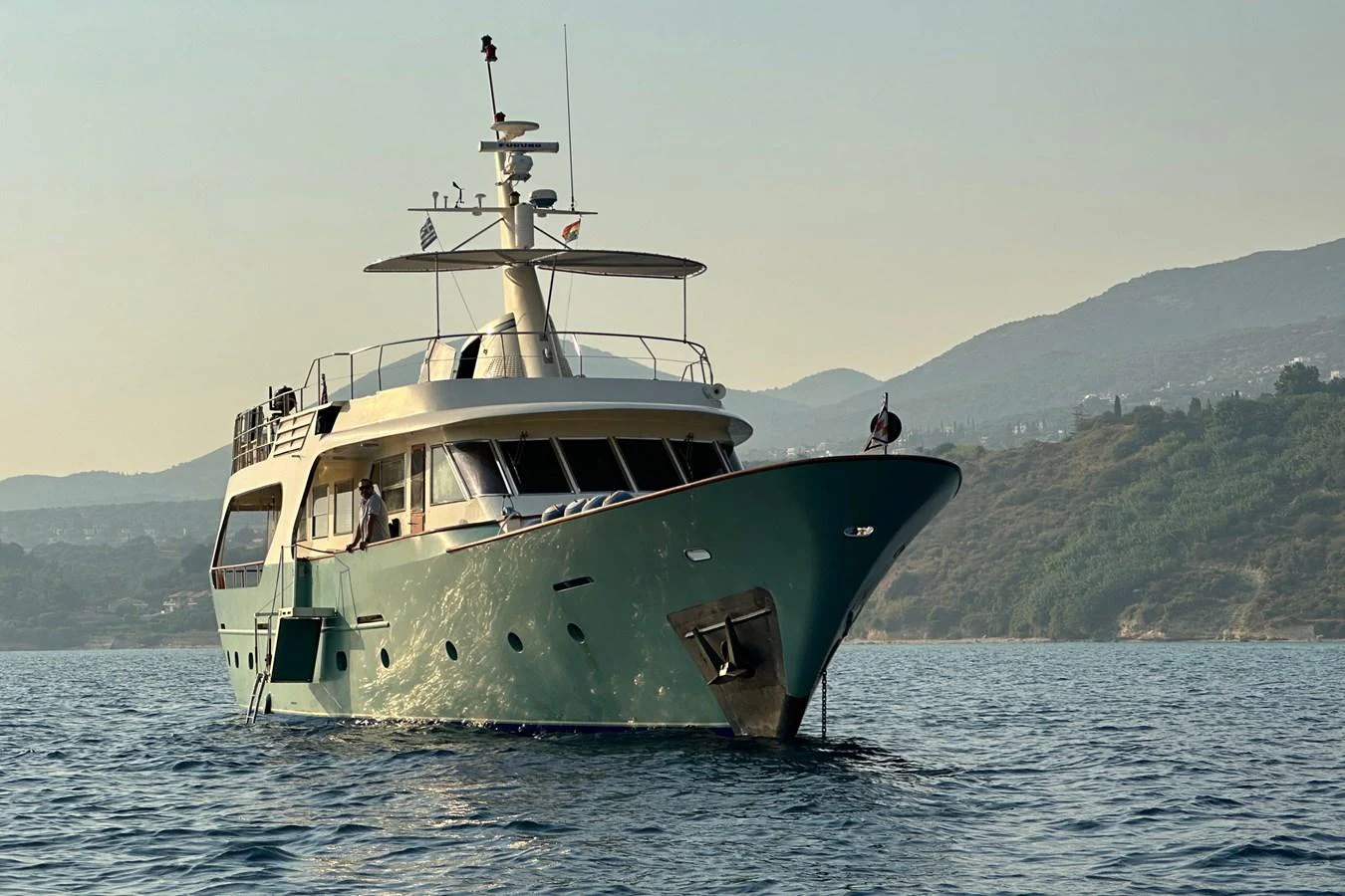 A luxurious yacht is anchored on calm waters with scenic hills in the background. aboard KALANI Yacht for Sale