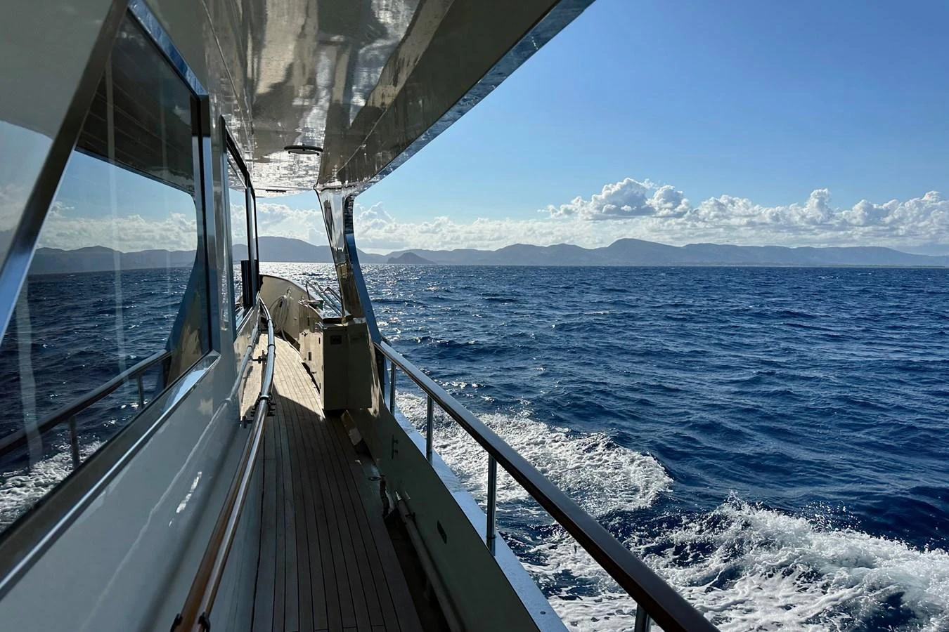 A serene view from the side deck of a yacht cruising on open waters under a clear blue sky. aboard KALANI Yacht for Sale